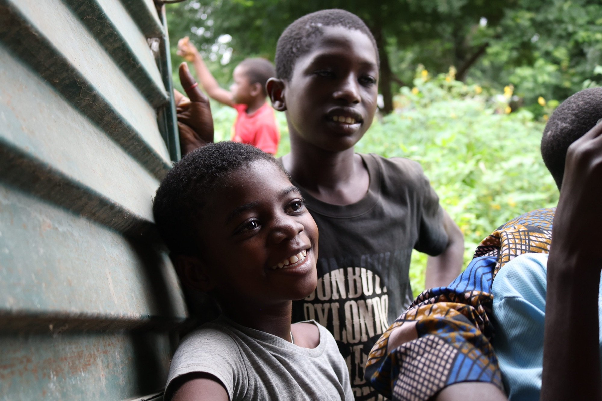 Two smiling boys lean against a building, one laughing toward the camera