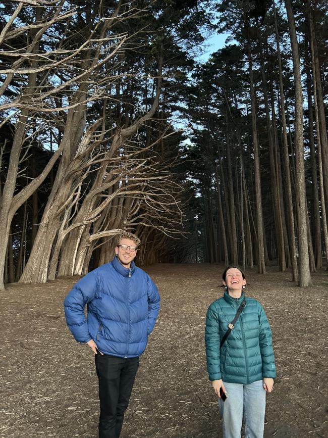 Maya and Phillip stand among tall windswept cypress trees