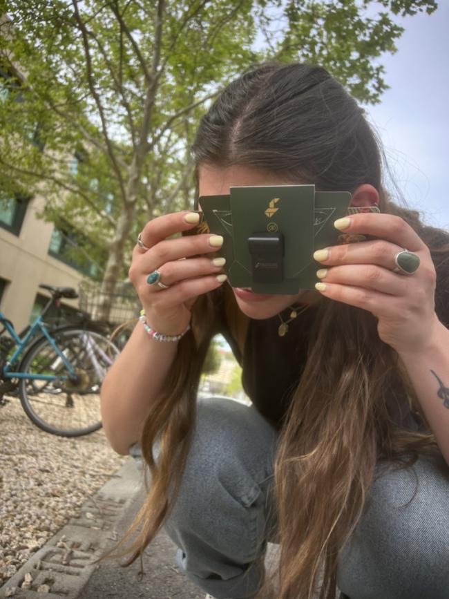 Maya crouches outdoors, looking through a small green Foldscope microscope held to one eye