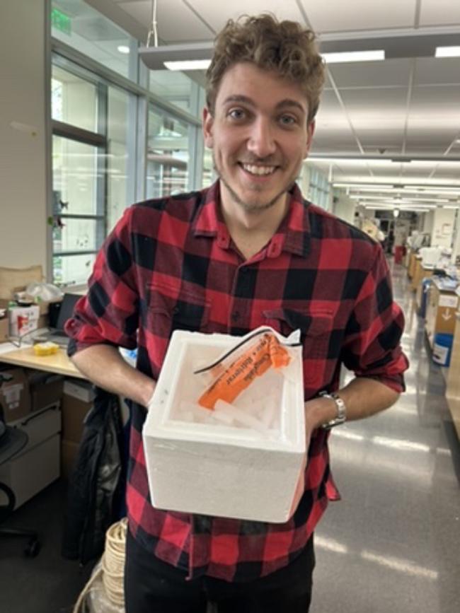 Phillip smiles holding a small styrofoam shipping box on dry ice