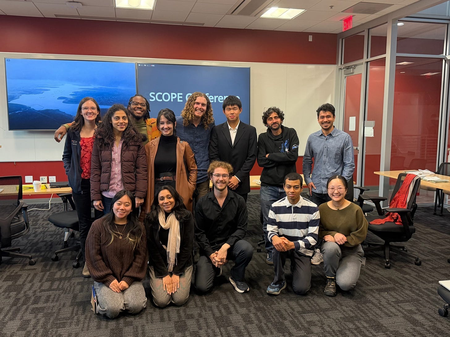 A group portrait of about fifteen students and researchers smiling in front of a screen reading SCOPE Conference