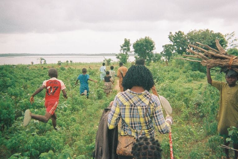 A group of researchers and community members walking a dirt path toward a river through green brush