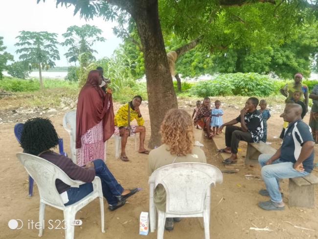 The team seated under a tree with community members at Imala Odo, discussing the study