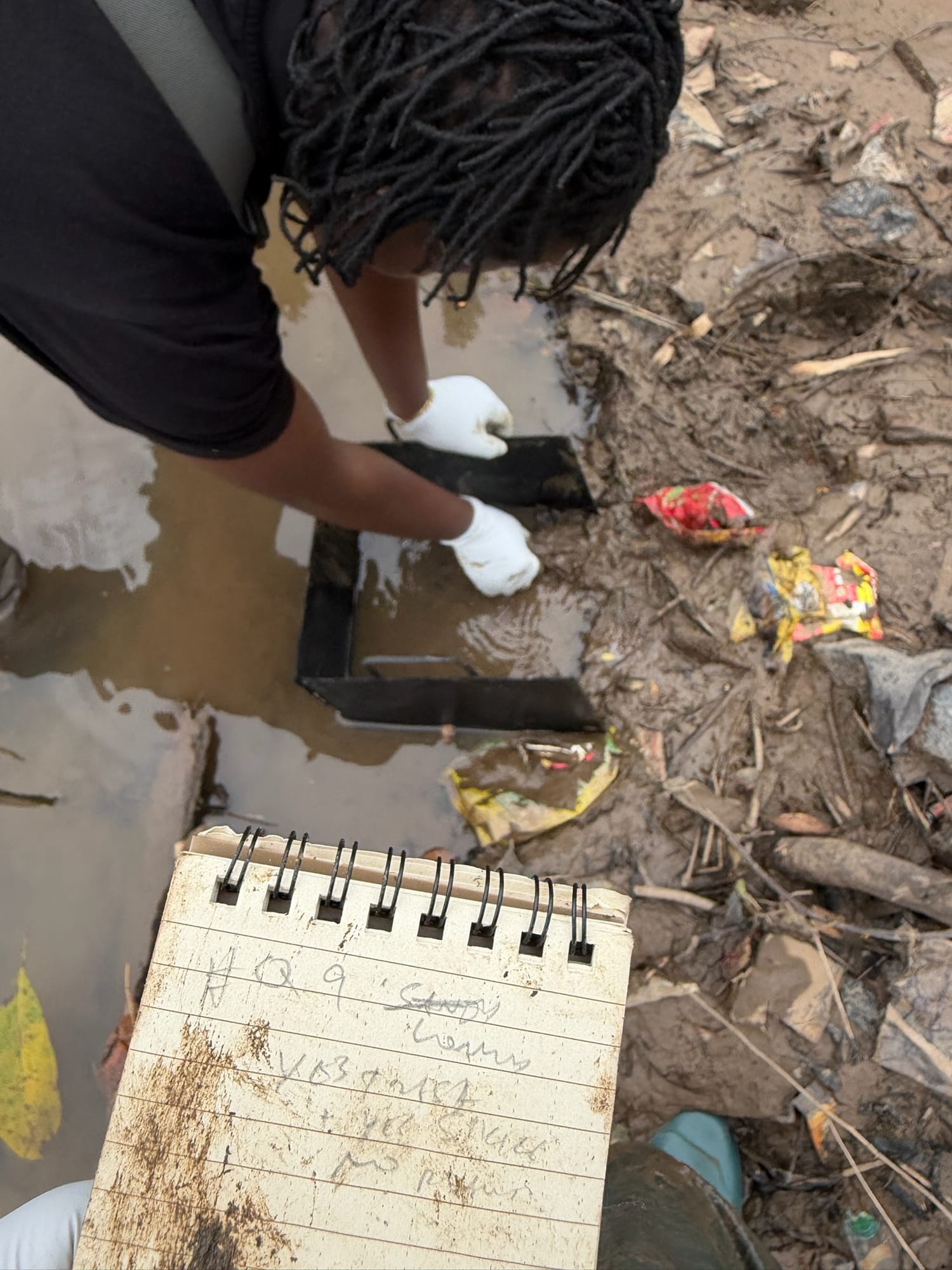 A quadrat laid in shallow muddy water beside a waterproof field notebook