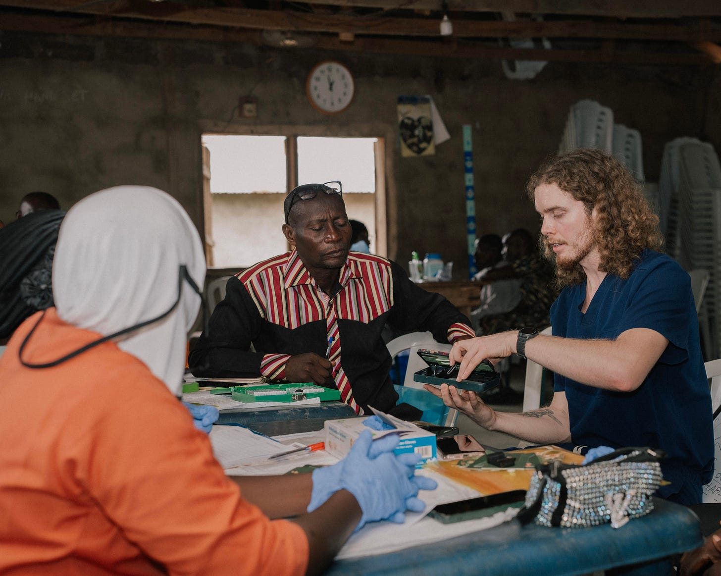 Will McCarthy shows a Foldscope kit to community members across a table in the schoolhouse clinic