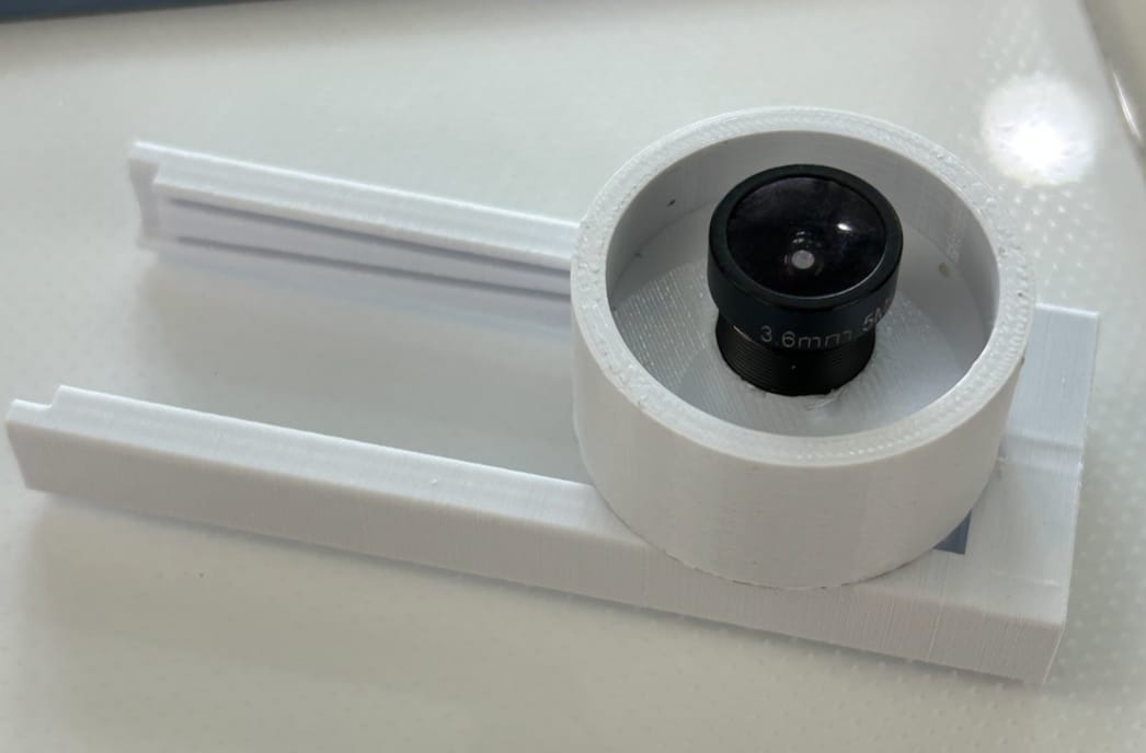 A black fish-eye lens seated in a white 3D-printed mount on a slider rail